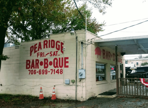 Exterior of Pea Ridge Bar-B-Que building with red signage, phone number, and surrounding trees.
