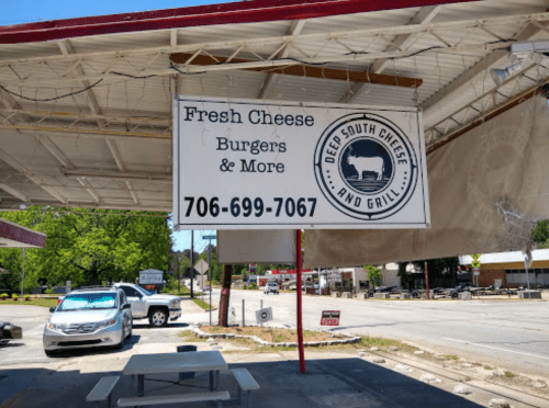 Sign for Deep South Cheese and Grill, advertising fresh cheese, burgers, and more, with a phone number and outdoor seating.