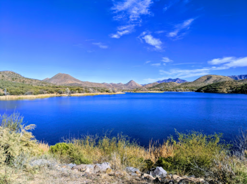 A serene lake surrounded by mountains and greenery under a clear blue sky.
