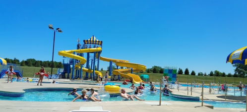 A sunny water park scene with yellow slides, a pool, and people enjoying the water and sun.