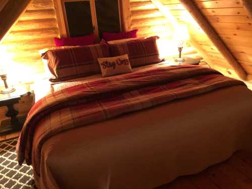 Cozy log cabin bedroom with a large bed, warm lighting, and rustic decor, featuring a "Stay Cozy" pillow.