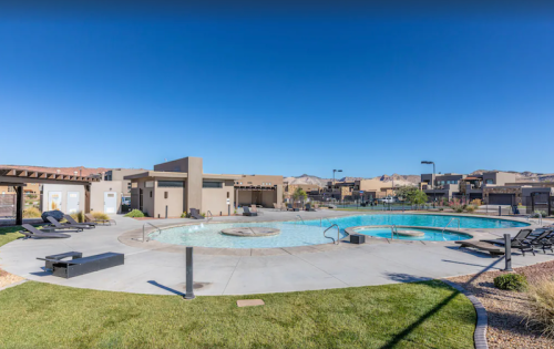 A sunny pool area with lounge chairs, a hot tub, and modern buildings in the background against a clear blue sky.