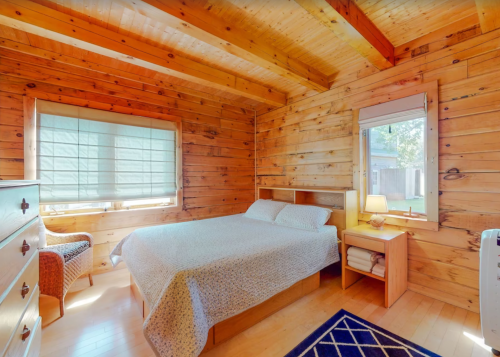 Cozy wooden bedroom with a double bed, natural light, and a small lamp beside a window.