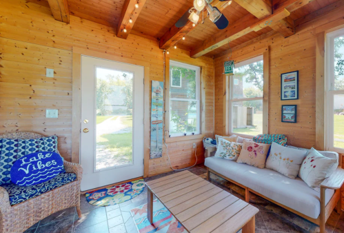 Cozy sunroom with wooden walls, a table, and comfortable seating, featuring decorative pillows and a door to the outdoors.