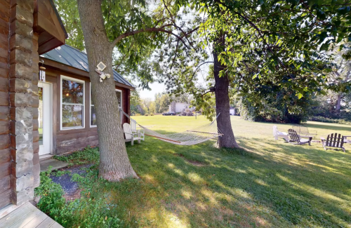 A peaceful outdoor scene featuring a hammock between two trees, a grassy area, and a cozy cabin.