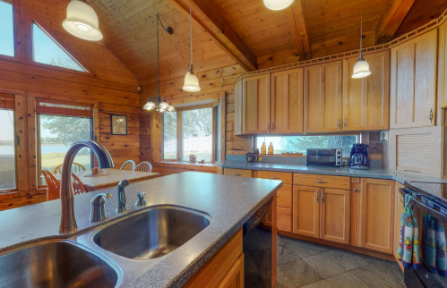 Cozy wooden kitchen with a large window, modern appliances, and a spacious countertop. Bright and inviting atmosphere.