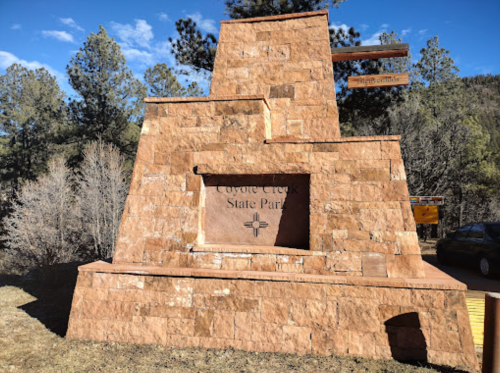 Sign for Coyote Creek State Park, featuring a stone structure with trees and a blue sky in the background.