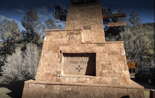 Stone monument with "Coyote Creek State Park" engraved, surrounded by trees and a clear blue sky.