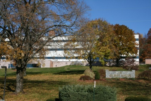 A school building surrounded by trees and grass, with autumn foliage and a sign that reads "Gilbert School."