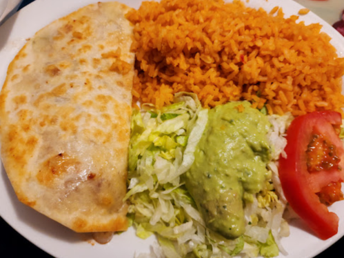 A plate of food featuring a quesadilla, orange rice, lettuce, guacamole, and tomato slices.
