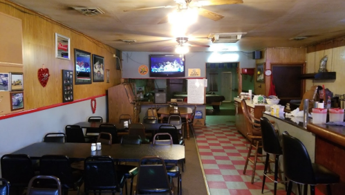 A cozy diner interior with tables, a bar, and a TV, featuring wooden walls and checkered flooring.