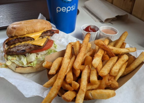 A cheeseburger with lettuce and tomato next to a serving of golden fries and a cup of Pepsi.