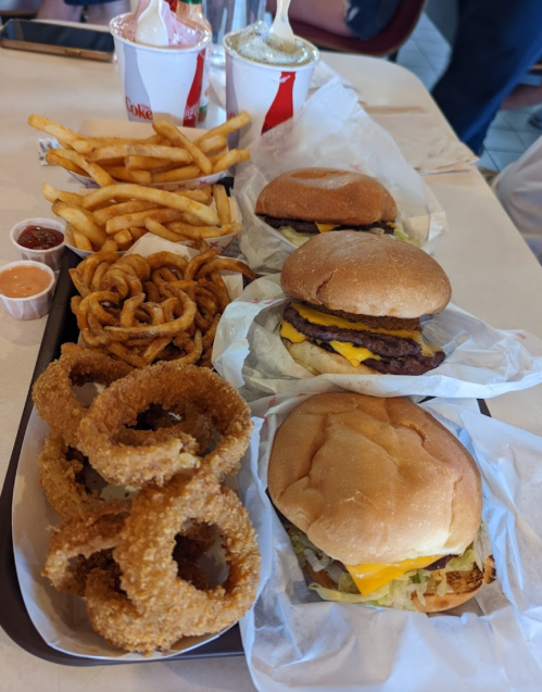 A tray of fast food featuring two cheeseburgers, onion rings, curly fries, and soft drinks.