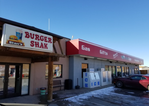 Exterior view of a building featuring "Burger Shak" and a gas station with gift shop signage under a clear blue sky.