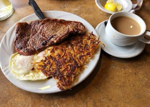 A plate with a steak, two fried eggs, crispy hash browns, and a cup of coffee on the side.
