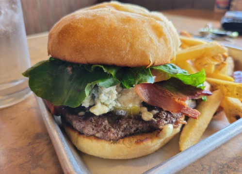 A juicy burger with lettuce, bacon, and blue cheese, served with a side of golden fries on a metal tray.