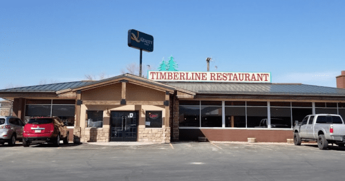 Exterior of Timberline Restaurant with a sign, large windows, and parked cars in the lot. Clear blue sky above.
