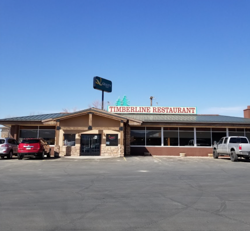 Exterior of Timberline Restaurant with a clear blue sky, featuring a parking lot and several parked cars.