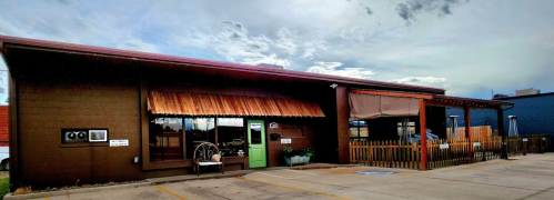 A brown building with a wooden awning, green door, and outdoor seating under a cloudy sky.