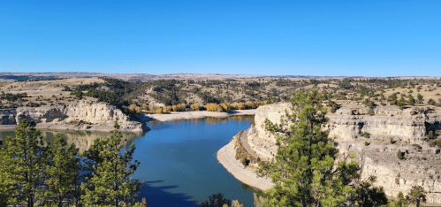 A scenic view of a river winding through rocky cliffs and green trees under a clear blue sky.