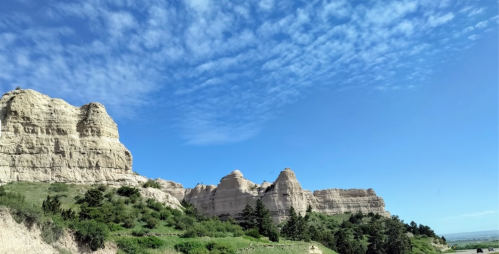 A scenic view of rugged cliffs and green vegetation under a bright blue sky with scattered clouds.