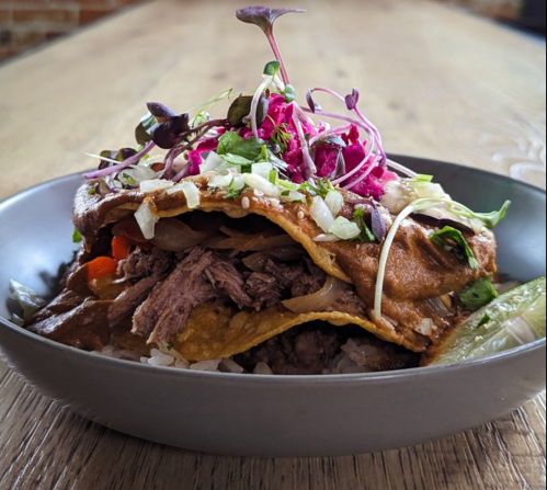 A bowl of layered tacos filled with beef, onions, and topped with fresh herbs and colorful vegetables.