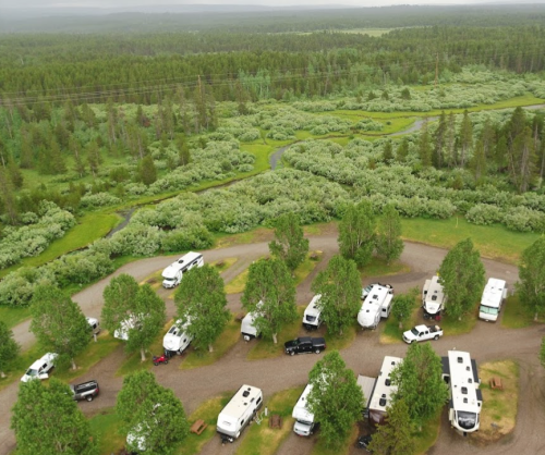 Aerial view of a campground with several RVs surrounded by lush greenery and a winding river.