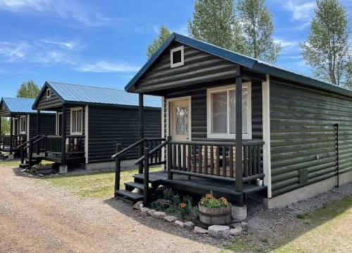 Three rustic cabins with blue roofs and wooden exteriors, set in a grassy area under a clear blue sky.