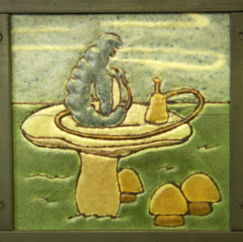 A ceramic tile featuring a blue caterpillar on a circular platform with a small vase and three mushrooms.
