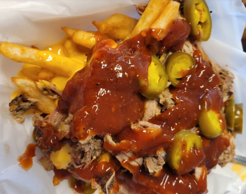 A plate of loaded fries topped with pulled pork, cheese, barbecue sauce, and jalapeños.