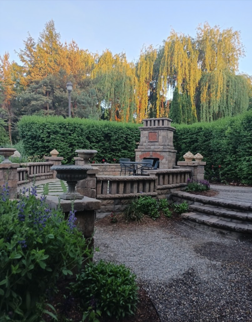 A serene garden with stone steps, a decorative wall, and lush greenery under a clear sky.