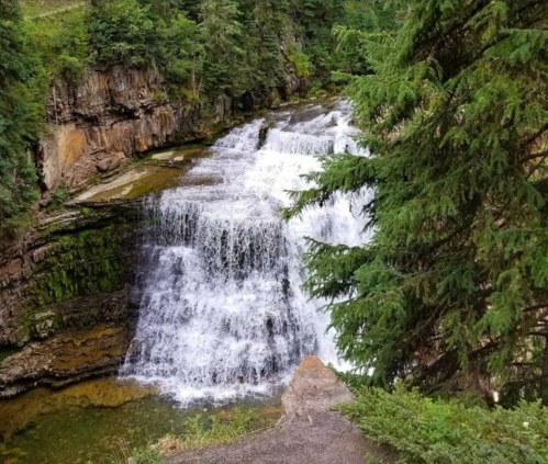A scenic waterfall cascading over rocky cliffs, surrounded by lush green trees and foliage.