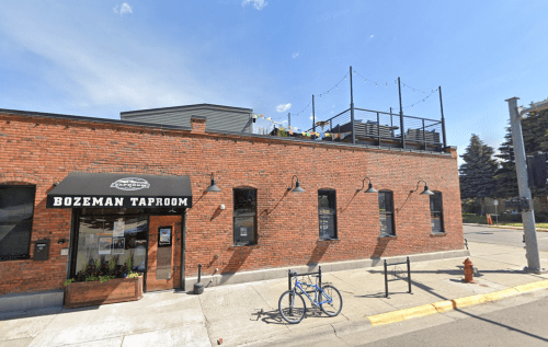 Exterior view of Bozeman Taproom, a brick building with a rooftop patio and a blue bicycle parked outside.