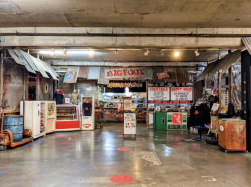 Interior of a rustic market with vintage decor, featuring signs for cocktails and happy hour, and a Bigfoot theme.