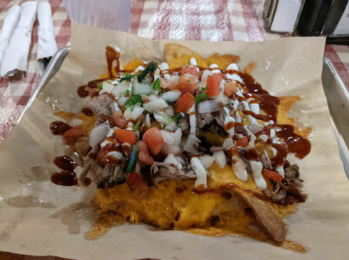 A tray of nachos topped with shredded meat, cheese, diced tomatoes, onions, and drizzled with sauce.