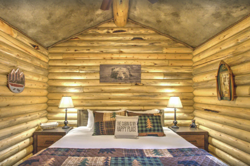 Cozy log cabin bedroom with a double bed, rustic decor, and warm lighting. A bear picture hangs on the wall.