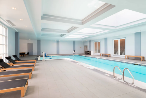 Indoor swimming pool area with lounge chairs, large windows, and a bright, modern design.