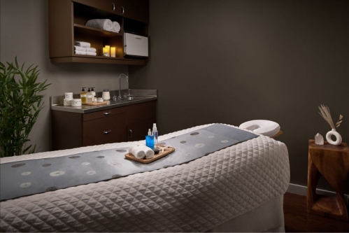 A serene spa treatment room featuring a massage table, soothing decor, and wellness products on a wooden tray.