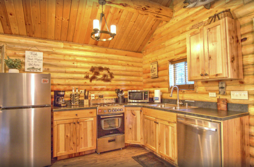 Cozy log cabin kitchen with wooden cabinets, stainless steel appliances, and warm lighting.