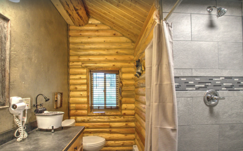 Cozy bathroom with log walls, a shower, sink, and window, featuring rustic decor and modern fixtures.