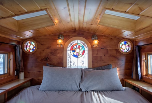 Cozy interior of a tiny home with wooden walls, skylights, and colorful stained glass windows.
