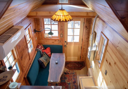 Cozy tiny house interior with wooden walls, a table, seating area, and a warm pendant light.