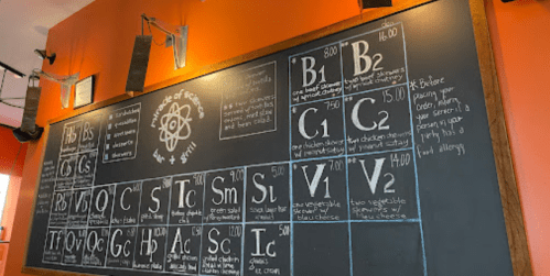 Chalkboard menu featuring a periodic table design with food items and prices listed in a casual eatery.