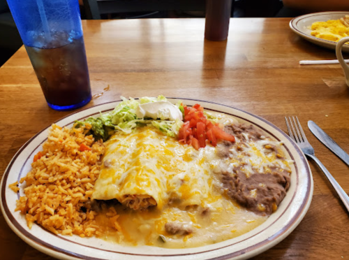 A plate of enchiladas topped with cheese, served with rice, refried beans, lettuce, tomatoes, and sour cream.