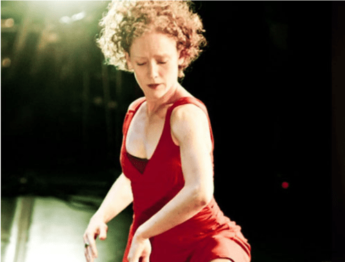 A dancer in a red dress performs on stage, captured in a moment of movement and expression.
