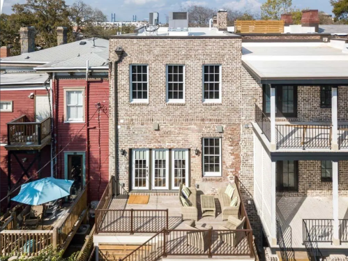 Aerial view of a brick building with large windows, a deck, and outdoor seating, surrounded by colorful neighboring structures.