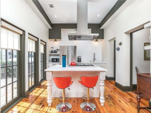 Modern kitchen with an island, red bar stools, stainless steel appliances, and natural light from large windows.