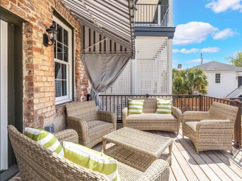 Cozy outdoor patio with wicker furniture and green-striped cushions, surrounded by brick walls and a sunny sky.