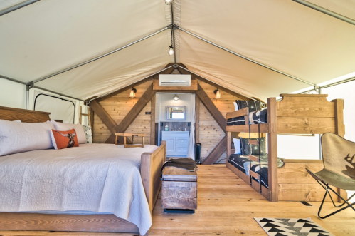 Cozy glamping tent interior featuring a double bed, bunk beds, and wooden accents. Bright and inviting atmosphere.