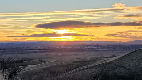A sunset over rolling hills, with vibrant orange and yellow hues illuminating the sky and landscape below.